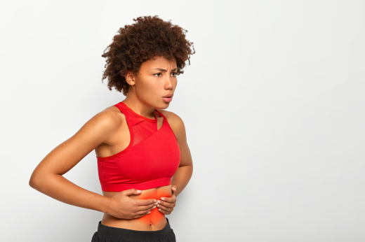 Imagem: Mulher de blusa vermelha, com expressão de dor, segurando a barriga