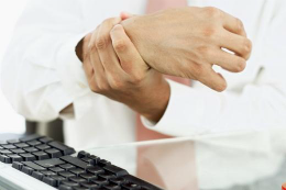 Imagem: Foto de pessoa apertando a própria mão próximo ao um teclado de computador