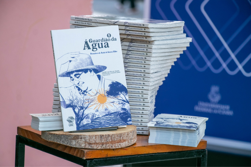 Imagem: Foto de exemplares empilhados do livro "O Guardião da Água" no estande da Editora UFC