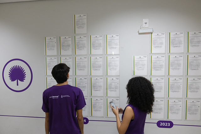 Fotografia de dois jovens observando mural com as cartas-patente concedidas à UFC (Foto: Victor Braga/UFC)