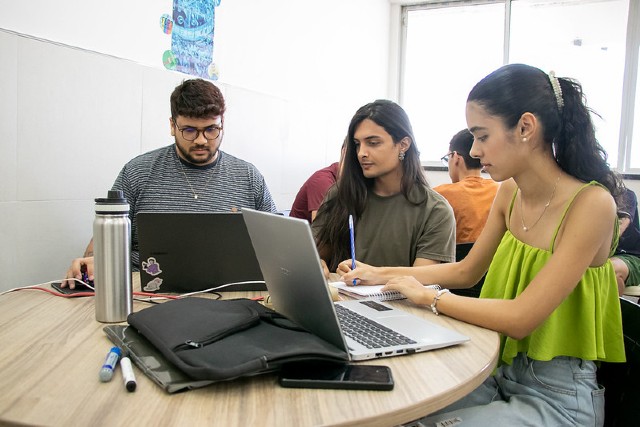 Imagem: Três estudantes sentados utilizando computadores em uma mesa