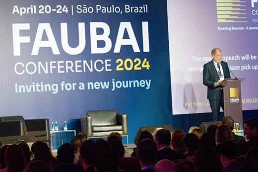 Imagem: De pé, na frente de um telão azul, o presidente da FAUBAI, José Celso Freire Junior, discursa na abertura do evento. (Foto: Divulgação/USP)