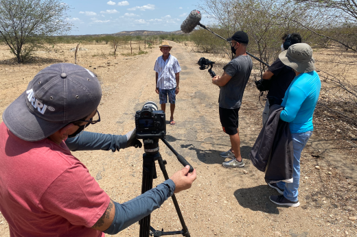 Imagem: Foto da equipe de filmagem do documentário entrevistando um morador de Jaguaribara gravando uma cena na paisagem da caatinga