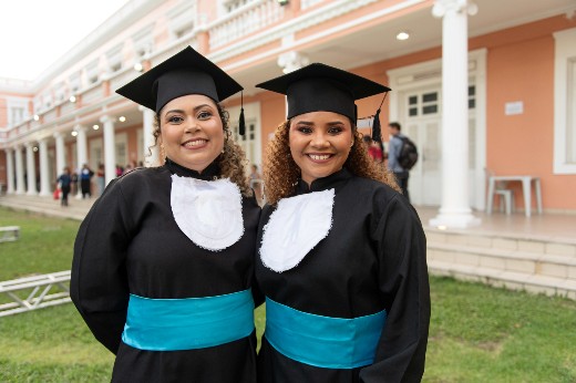 Estudantes Carla e Laís trajando beca no jardim da Reitoria