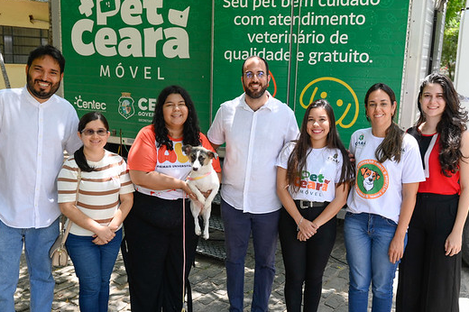 Na imagem, há um grupo de oito pessoas sorrindo e posando para a foto em frente a um veículo com o logotipo "Pet Ceará Móvel". Esse veículo parece oferecer serviços veterinários gratuitos, conforme indicado pelas palavras escritas na lateral, como "atendimento veterinário de qualidade e gratuito".  A maioria das pessoas está vestida com roupas casuais, algumas com camisetas relacionadas ao projeto Pet Ceará. Uma mulher no centro está segurando um cachorro, que também está olhando para a câmera. O grupo aparenta ser parte da equipe responsável pelo projeto, já que estão ao lado do veículo com a marca do serviço.