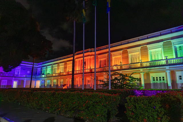 Foto da fachada do prédio da Reitoria da UFC iluminada com as cores do arco-íris