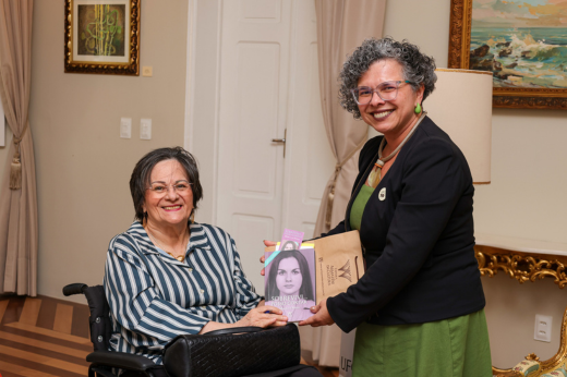 Imagem: A vice-reitora Diana Azevedo recebe um livro das mãos de Maria da Penha