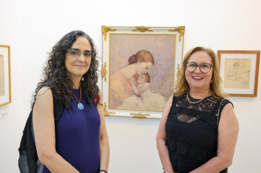 Imagem: Foto posada das pesquisadoras Márcia Castro e Márcia Machado em frente a um quadro com uma mãe segurando um bebê, de autoria do pintor Raimundo Cela