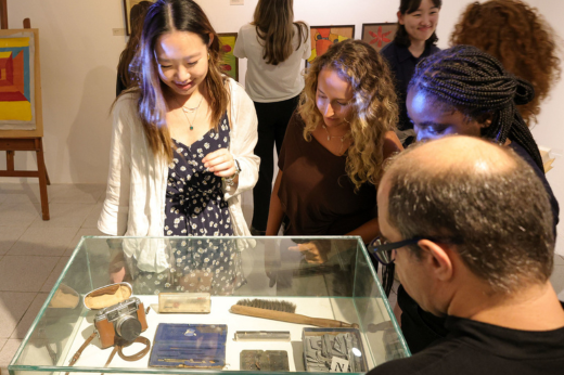 Imagem: alunas vendo a exposição no MAUC com uma redoma de vidro com objetos típicos de um escritório de arquitetura