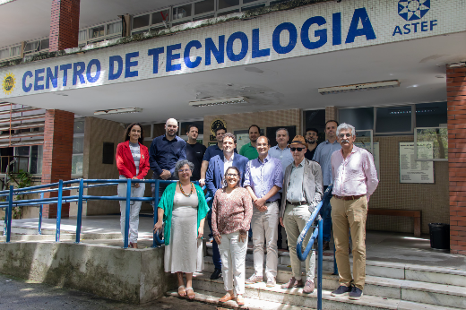 Imagem: Foto mostra os professores e professoras presentes à visita em frente ao bloco do Centro de Tecnologia da UFC. Eles estão nos degraus da escada que dá acesso ao campus, de pé, e acima deles se vê o nome Centro de Tecnologia 