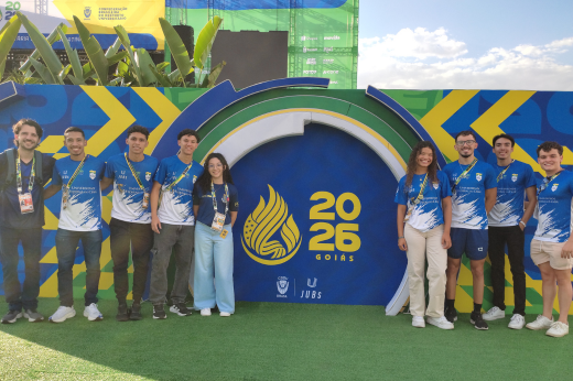 Painel do JUBs 2026 e estudantes abraçados lateralmente de um lado e do outro do painel