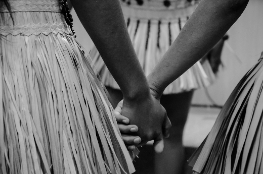 Fotografia em preto e branco de close de duas pessoas indígenas dando as mãos