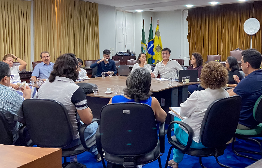 Imagem: Foto mostra um grupo de pessoas reunidos, sentados em torno de uma mesa, tendo o reitor da UFC, Professor Custódio Almeida, no fundo, ao centro da imagem (Foto: Guilherme Silva/UFC Informa)