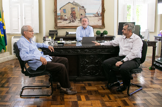 Imagem: três homens conversam em torno de uma mesa