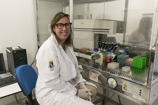 Imagem: A Profª Cláudia do Ó Pessoa sentada frente a um equipamento de laboratório