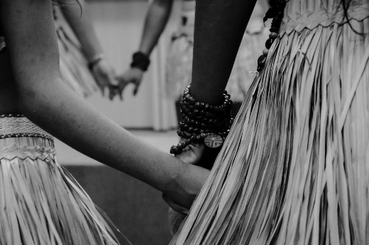 Detalhe de mulheres indígenas de mãos dadas, enquanto dançam com vestes de sua etnia