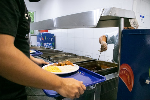 Imagem: estudante segura bandeja com prato à espera de ser servido no restaurante universitário