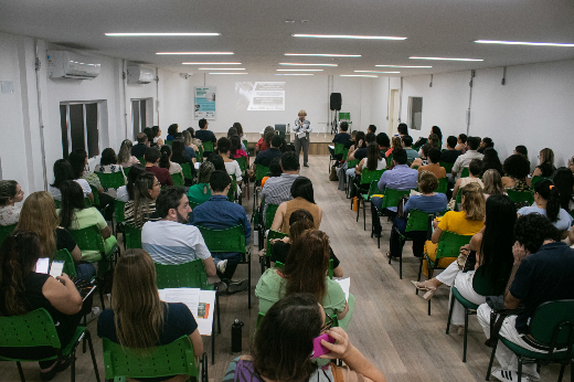 Imagem: pessoas sentadas em cadeiras ouvem palestra em auditório