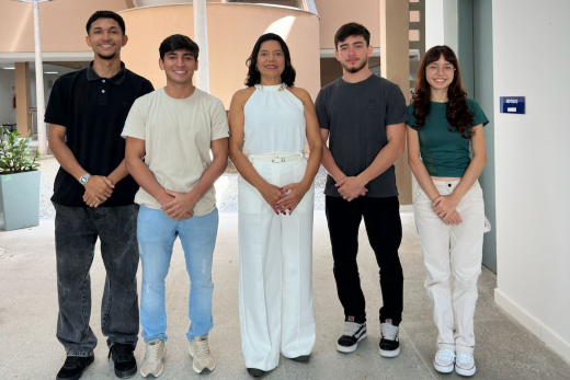 Imagem: da esquerda para a direita, vemos integrantes da startup Bimp, em foto onde aparecem de pé, na seguinte ordem: Jamesson Alberto (blusa polo preta), Pedro Levi (blusa bege), Prof Márcia Rodrigues (macacão branco), Assis Paiva (blusa cinza), Sarah Paiva (blusa verde)