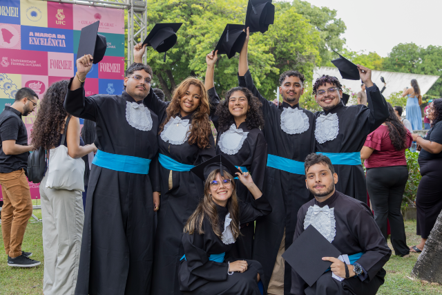 Imagem: Estudantes nos jardins da Reitoria da UFC com traje de beca durante cerimônia de Colação de Grau